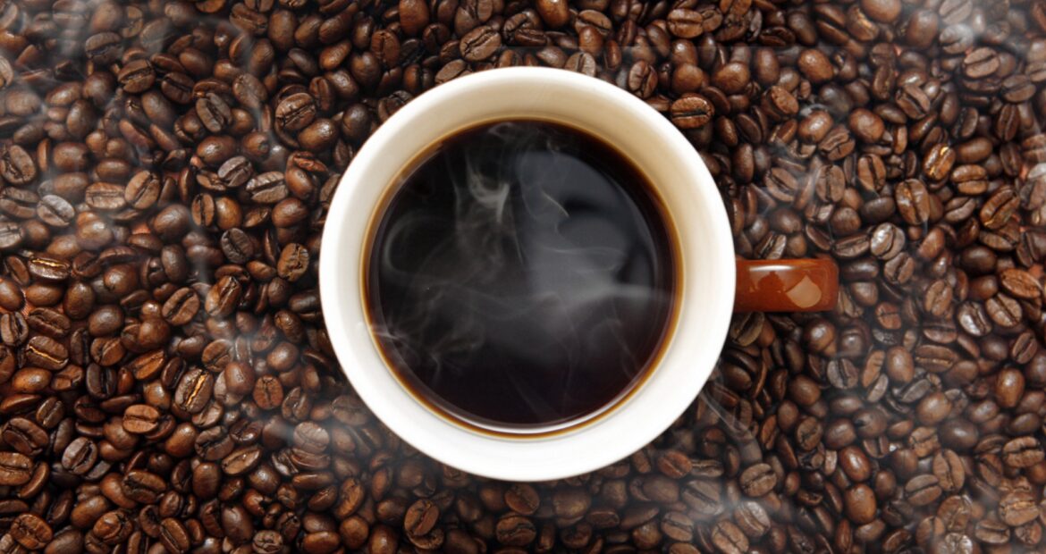 This is a photo of a cup of black coffee surrounded by coffee beans.